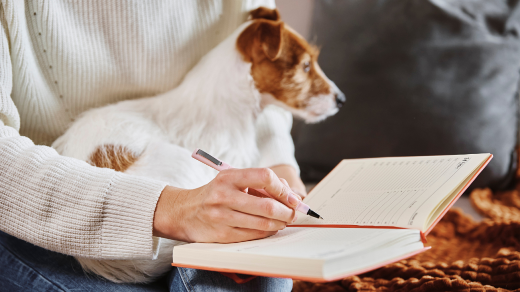 Vet visit preparation — Christian woman journaling notes with her dog beside her before an appointment.